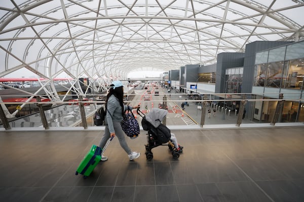 A person pushing a stroller walks through the pedestrian bridge at the North Terminal at Hartsfield-Jackson International Airport ahead of Christmas on Thursday, Dec. 22, 2022. During peak holiday times, travelers may encounter long lines at airline ticket counters to check bags. (Miguel Martinez/AJC)