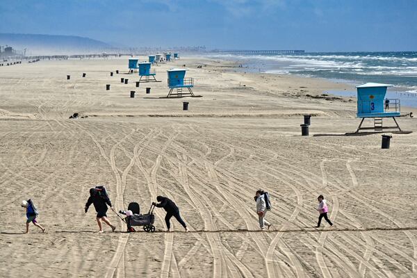 Beach goers trudge through the sand in a windy day south of the pier in Huntington Beach, Calif., Thursday, March 13, 2025, after strong storms moved through the region overnight. (Jeff Gritchen/The Orange County Register via AP)