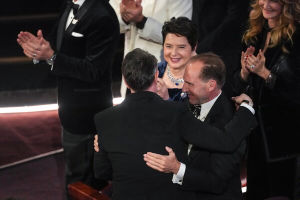 Isabella Rossellini, center, and Ralph Fiennes, right, congratulates Peter Straughan, left, as he wins the award for best adapted screenplay for "Conclave" during the Oscars on Sunday, March 2, 2025, at the Dolby Theatre in Los Angeles. (AP Photo/Chris Pizzello)