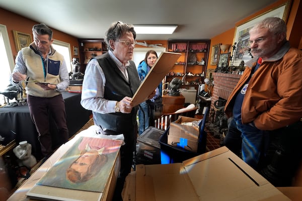 Appraiser Kaja Veilleux examines a painting brought in by Wanda Morris, background, and her husband, Jeff Morris, right, while associate appraiser Darrin Guitreau, left, takes notes, at Thomaston Place Auction Galleries, Tuesday, Nov. 19, 2024, in Thomaston, Maine. (AP Photo/Robert F. Bukaty)