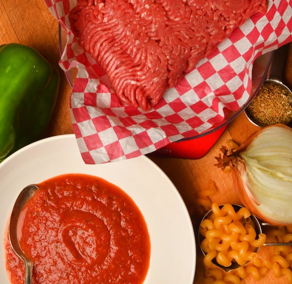 Pasta Meat Sauce (left in dish with spoon) with ingredients (clockwise from left): green bell pepper, ground sirloin, Italian Spice Blend, yellow onion and cellentani pasta. 
(Styling by Jennifer Hill Booker / Chris Hunt for the Atlanta Journal-Constitution)