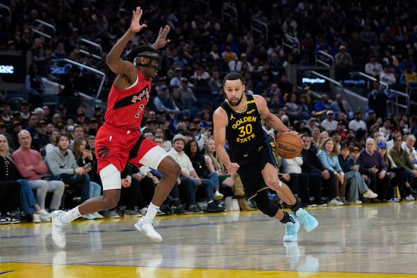 Golden State Warriors guard Stephen Curry (30) moves the ball next to Toronto Raptors forward Jonathan Mogbo (2) during the first half of an NBA basketball game Thursday, March 20, 2025, in San Francisco. (AP Photo/Godofredo A. Vásquez)