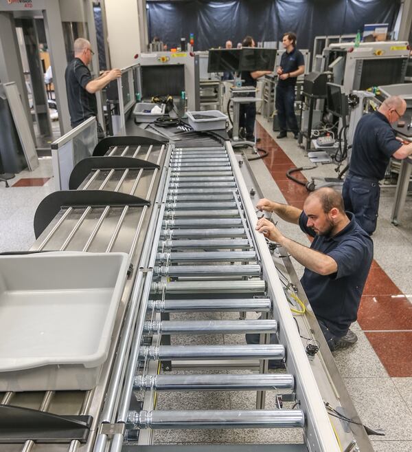 A new lane while it was under construction in early May. The stations on the left allow five different travelers to load bins, each at their own pace. After loading a bin, the traveler pushes the bin onto the automated conveyor system on the right, which will shuttle the bin to the X-ray machine. The passenger can then walk through screening without waiting for slower passengers in front to finish loading bins. John Spink / AJC