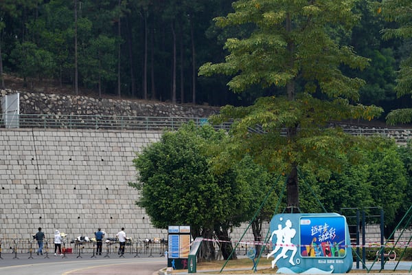 Volunteers relocate flowers laid outside "Zhuhai People's Fitness Plaza" to a barrier leading into the area where a man rammed his car into people exercising at the sports center, in Zhuhai in southern China's Guangdong province on Wednesday, Nov. 13, 2024. (AP Photo/Ng Han Guan)