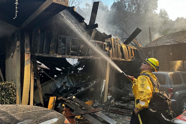 A firefighter hoses down hot spots around a fire-ravaged property after the Franklin Fire swept through Tuesday, Dec. 10, 2024, in Malibu, Calif. (AP Photo/Eugene Garcia)