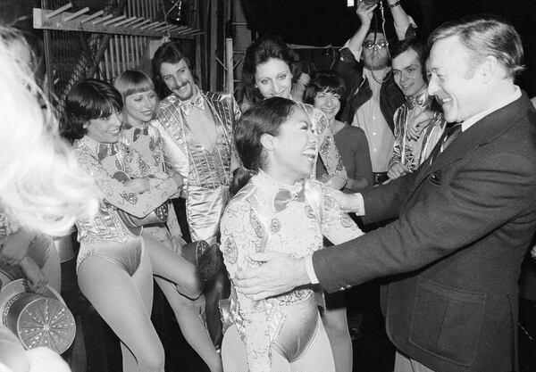 Dancer Gene Kelly, right, embraces Baayork Lee, cast member of the musical "A Chorus Line" backstage at New York's Shubert Theater, Nov. 19, 1975. Miss Lee had been in the cast of the musical "Flower Drum Song" which Kelly had directed on Broadway. Other "Chorus Line" cast members look on. (AP Photo/Richard Drew)