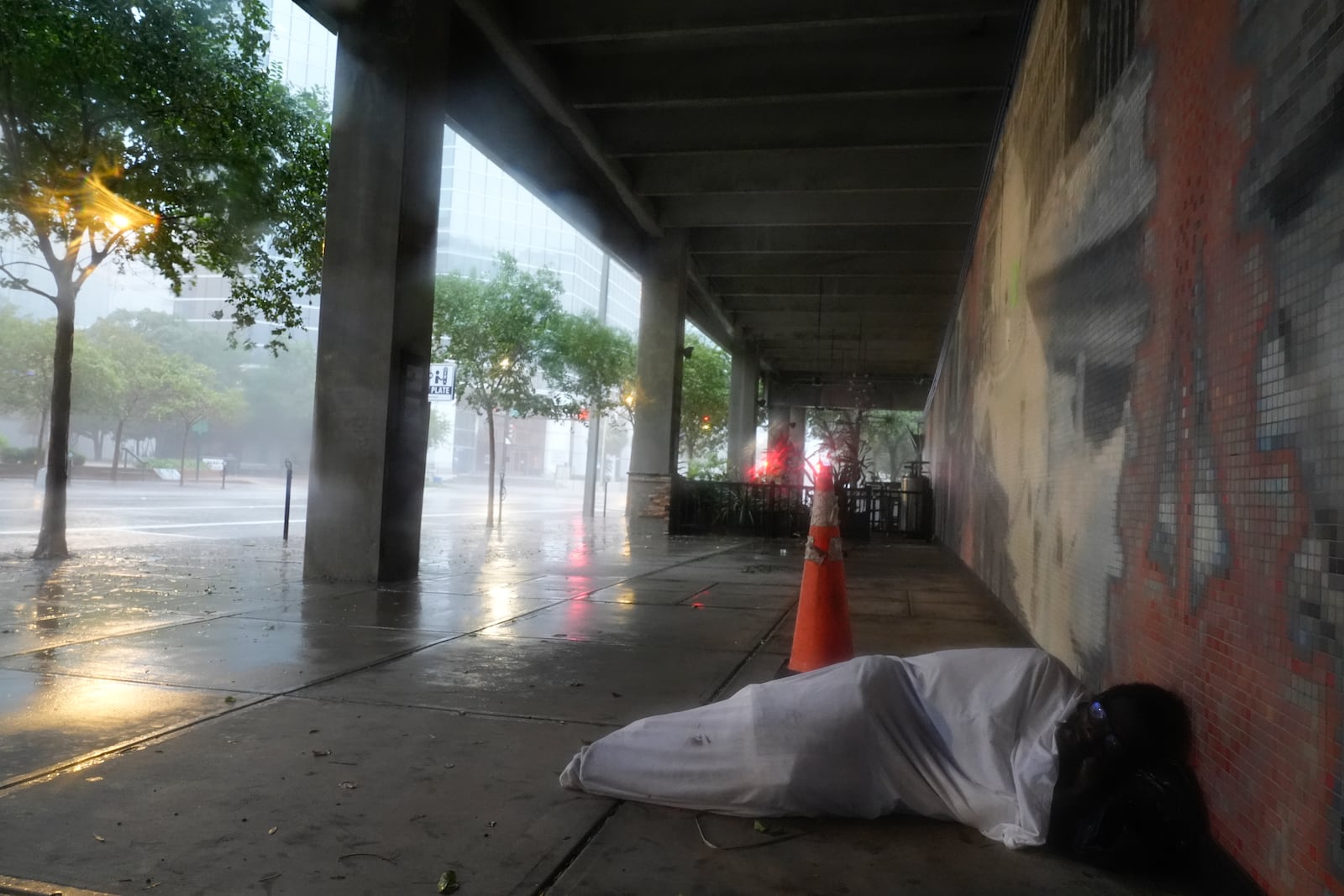 Melvin Lee Hicks, who is homeless, lies under a sheet donated by a nearby hotel, as he shelters alongside a parking garage in downtown Tampa, Fla., during the approach of Hurricane Milton, Wednesday, Oct. 9, 2024. (AP Photo/Rebecca Blackwell)