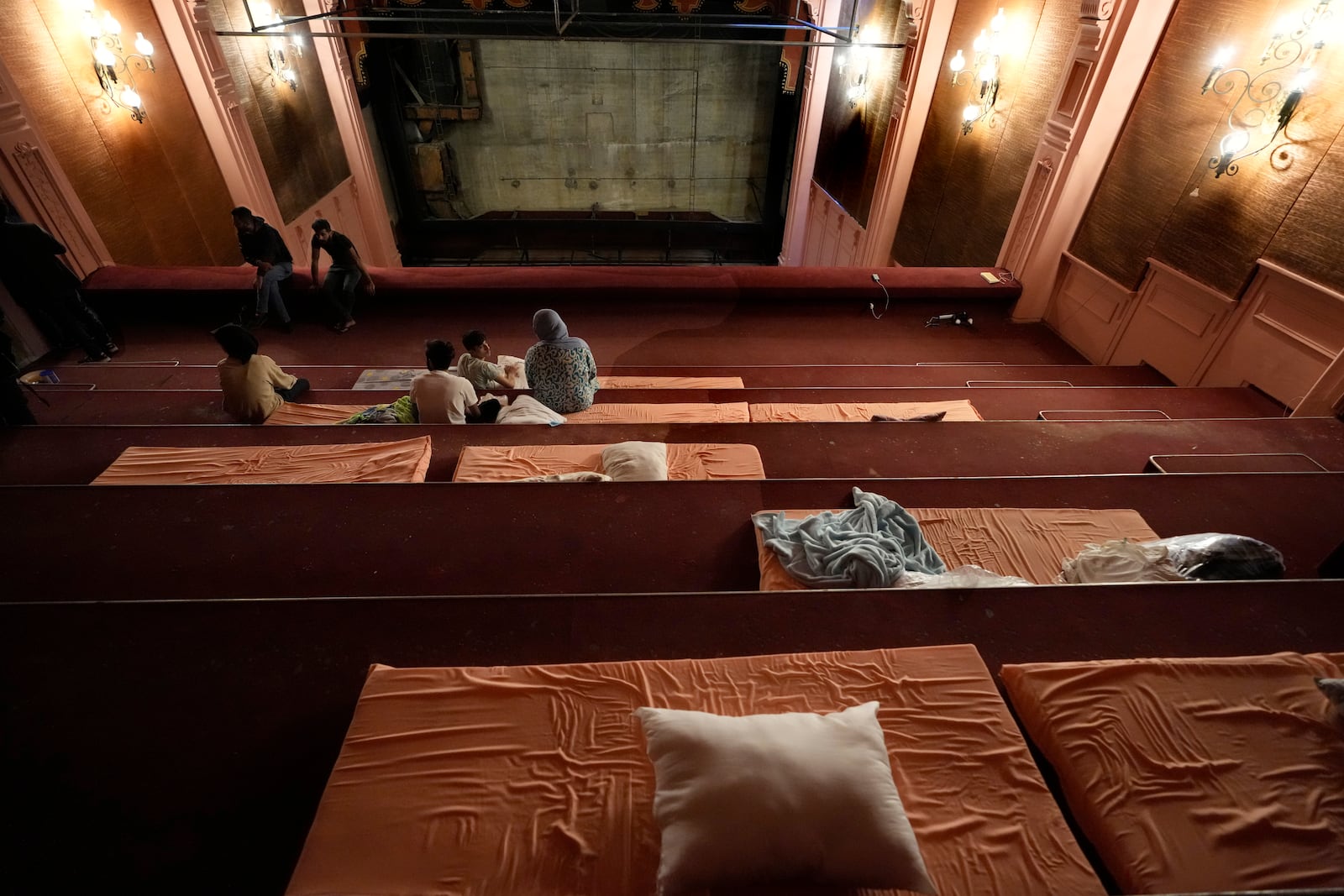 A displaced family who fled the ongoing Hezbollah-Israel war in south Lebanon, sit on mattresses inside one of Beirut's oldest and best known movie theatres, Le Colisee, in Beirut, Lebanon, Tuesday, Oct. 22, 2024. (AP Photo/Hussein Malla)