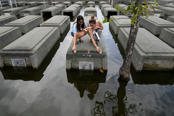 Women place candles on the half-submerged tomb of family members at flood-prone Holy Spirit Memorial Park in Masantol, Pampanga province, Philippines after heavy rains from recent tropical storm Trami caused water to become higher than usual, ahead of All Saints Day, Thursday Oct. 31, 2024. (AP Photo/Aaron Favila)