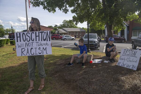 Hoschton resident Kelly Winebarger protests for the resignation of Hoschton Mayor Theresa Kenerly and Councilman Jim Cleveland as her sons Ryder (center) and Knox (right) sit quietly by the roadside in Hoschton, Monday, May 6, 2019. “I don’t want people the think that about our community,” Kelly said as she referenced the controversy concerning the mayor of Hoschton allegedly pulling the resume of Keith Henry from a packet of four finalists for a city position, “because he is black, and the city isn’t ready for this.”(ALYSSA POINTER/ALYSSA.POINTER@AJC.COM)