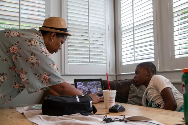 C3 Academics pod leader Ashli Colbert (left) checks the battery on Howard Middle School eighth grader Jahson Jahi's computer while he participates in virtual classes in Atlanta on Friday, August 28, 2020. (Alyssa Pointer / Alyssa.Pointer@ajc.com)