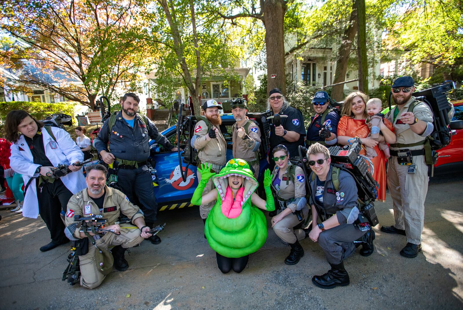 The Atlanta Ghostbusters gather in front of an Ectomobile replica on Euclid Avenue before the annual Little 5 Points Halloween Parade on Sunday, Oct 20, 2024. The group includes (from left) TJ Scheitler, Dustin Grau, Joseph Ricciardelli, Jonathan Mitchell, Jonathon McCoy, Brad Peters, Kevin Looney, Chelsea Ritter-Jones holding 8-month old Logan Jones, Marcus Jones, Cara Davis as Slimer (center front), Carolyn Hinkle and Neil Hinkle. (Jenni Girtman for the AJC)