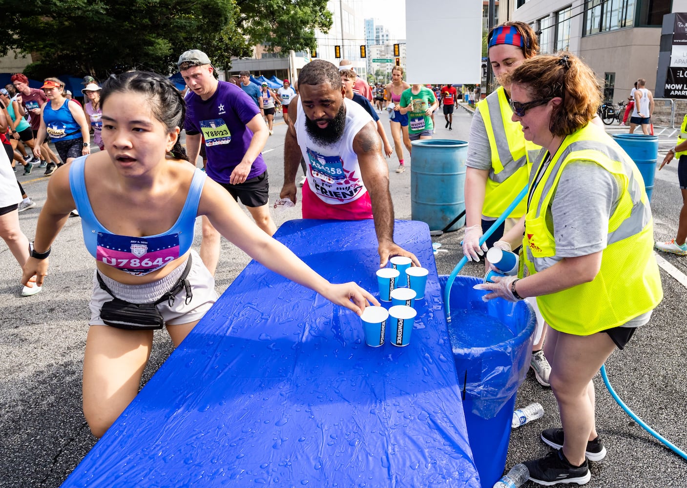 Atlanta Track Club volunteers fill cups of water for runners to take during the 55th running of The Atlanta Journal-Constitution Peachtree Road Race at "Cardiac Hill" on Peachtree Road NW in Atlanta on Thursday, July 4, 2024. (Seeger Gray / AJC)