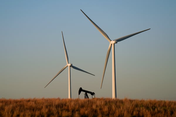 FILE - An oil pumping unit works in the foreground while wind turbines at the Buckeye Wind Energy wind farm rise in the distance Sept. 30, 2024, near Hays, Kan. (AP Photo/Charlie Riedel, File)