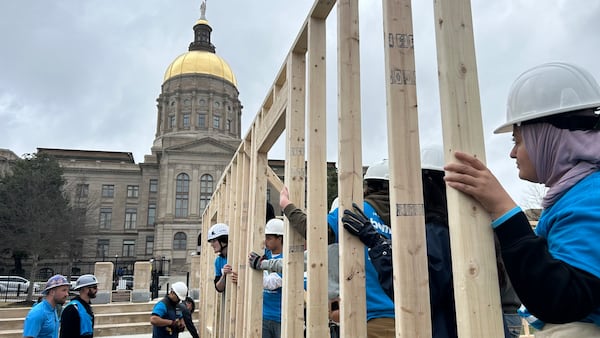 A line of volunteers holding a portion of wooden housing frame in front of the Georgia capitol.