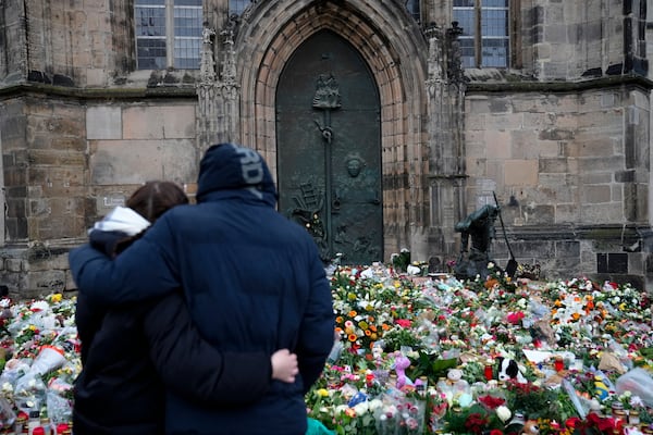 A couple embrace each other in front of flowers and candles laid down at the Johannis church close to the Christmas market, where a car drove into a crowd on Friday evening, in Magdeburg, Germany, Sunday, Dec. 22, 2024. (AP Photo/Ebrahim Noroozi)