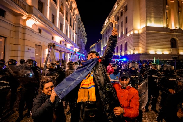 A woman screams holding a cross in front of riot policemen blocking a street following clashes with supporters of Calin Georgescu after Romania's electoral body rejected his candidacy in the presidential election rerun in Bucharest, Romania, Monday, March 10, 2025. (AP Photo/Andreea Alexandru)