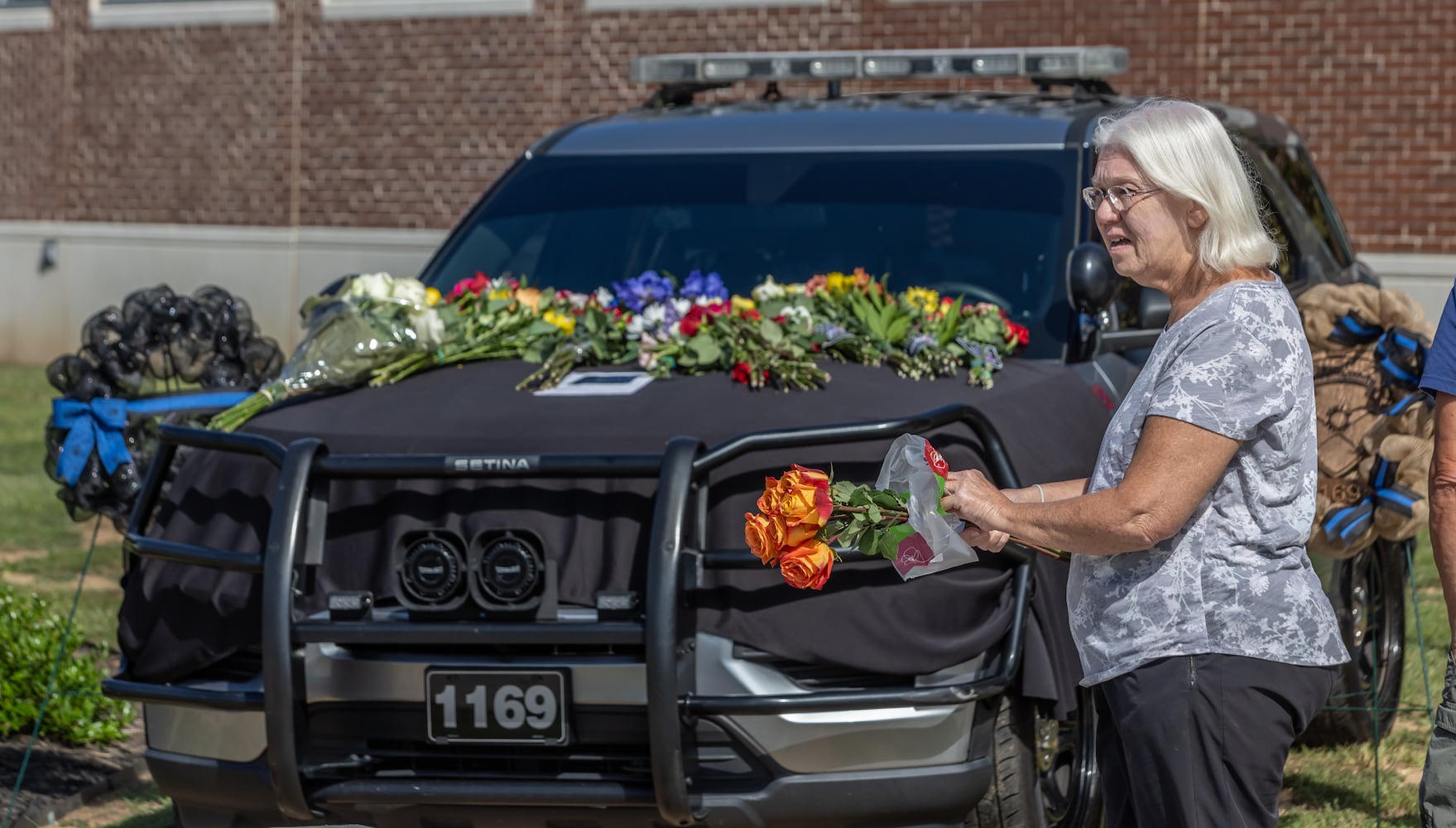 Linda Bohnn prepares to lay flowers on the patrol car in front of the Paulding County sheriff’s office. “The patrol car is here to give our community a place to publicly mourn,” Major Ashley Henson said. “The outpouring of support has been monumental and we’re so blessed to have such a great community.” (John Spink/AJC)