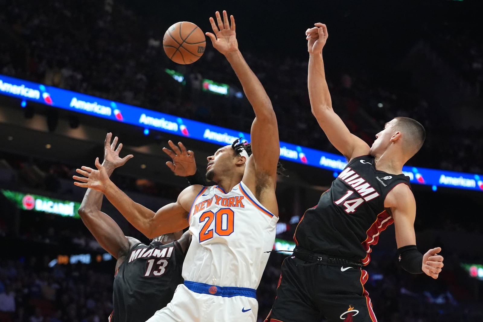 New York Knicks center Jericho Sims (20) goes for a loose ball against Miami Heat center Bam Adebayo (13) and Miami Heat guard Tyler Herro (14) during the first half of an NBA basketball game, Wednesday, Oct. 30, 2024, in Miami. (AP Photo/Lynne Sladky)