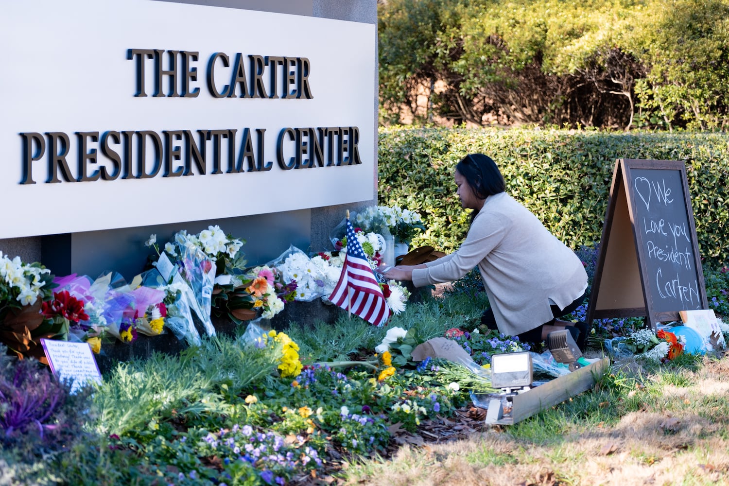 Jansen Head, of Woodstock, places a rosary on a makeshift memorial to former President Jimmy Carter at the Carter Center in Atlanta on Monday, Dec. 30, 2024.   Ben Gray for the Atlanta Journal-Constitution