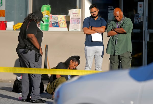 A medical examiner looks over a body at the scene of a shooting in the parking lot of a Chevron station at the corner of Monroe Drive and Piedmont Road in Atlanta on June 21, 2021. A rideshare driver opened fired at the gas station, killing one passenger and injuring another.(Christine Tannous / christine.tannous@ajc.com)