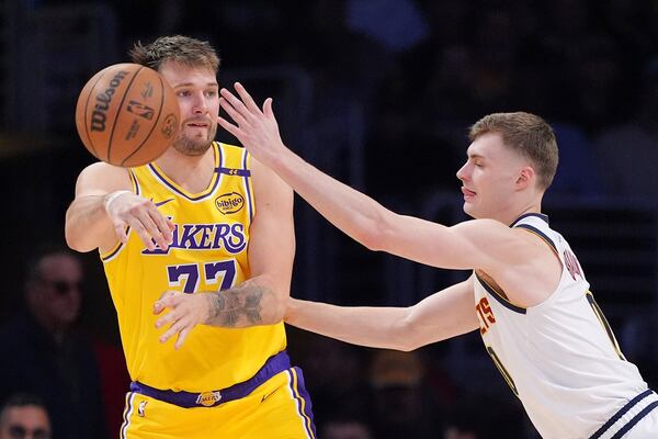 Los Angeles Lakers guard Luka Doncic, left, passes while under pressure from Denver Nuggets guard Christian Braun during the second half of an NBA basketball game Wednesday, March 19, 2025, in Los Angeles. (AP Photo/Mark J. Terrill)