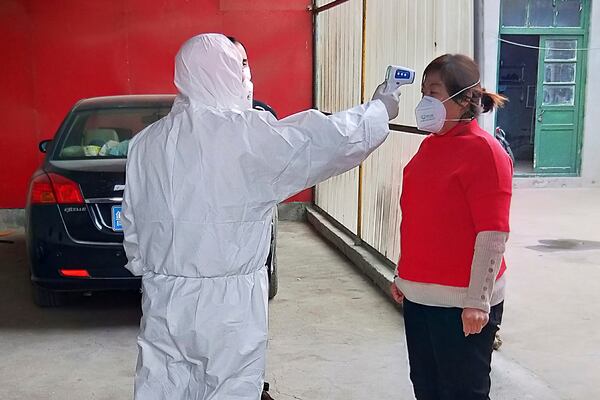 A government worker in a protective suit checks the temperature of a person under home quarantine in Shandong Province.