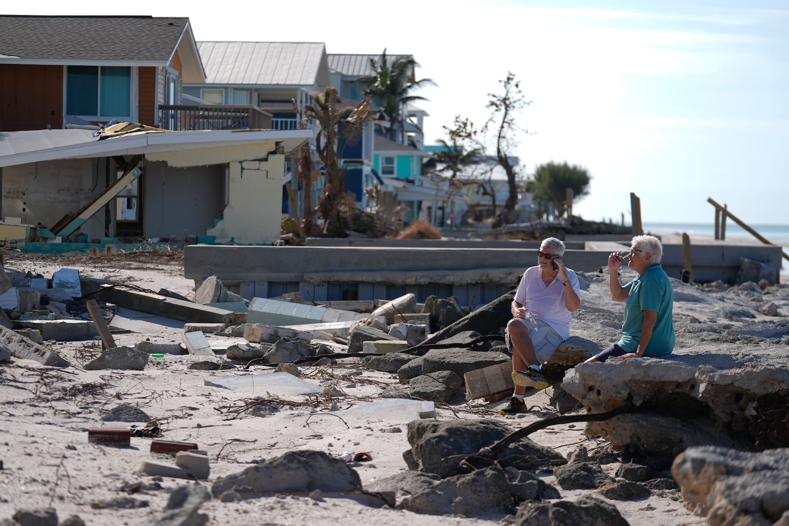 Property owners who preferred not to be named sit on the torn-up beach near their beachfront home and business, which was damaged in Hurricane Helene and then destroyed in Hurricane Milton, on Manasota Key, in Englewood, Fla., following the passage of Hurricane Milton, Sunday, Oct. 13, 2024. (AP Photo/Rebecca Blackwell)