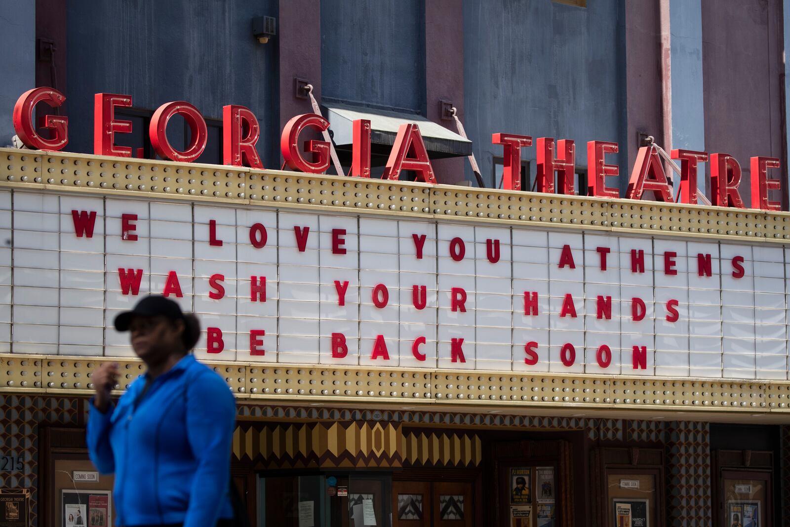 A woman walks past the Georgia Theatre Friday, March 20, 2020, in downton Athens, Ga. A note posted on the theatre's door says they are close and all shows are postponed. (AP Photo/John Bazemore)