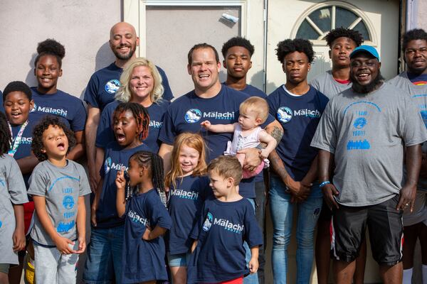 Pastor Terrell Scott(center), his family and volunteers with the Malachi Project pose in front of the home that will be turned into a community center in the McDonough Housing Authority Complex. PHIL SKINNER/FOR THE AJC