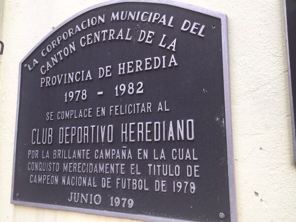 A plaque commemorating the stadium and team is affixed to a wall that you walk by as you enter the stadium  from a corner near the street. The field is ahead.