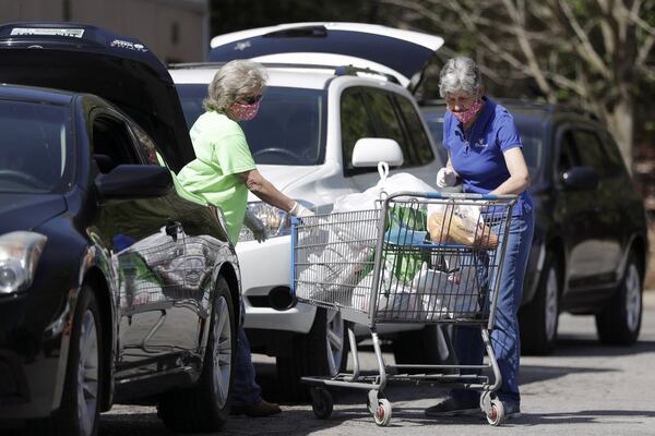 workers Nellie King, left, and Sylvia Ware, right, load food and supplies into a family's trunk at GraceWorks Ministries food pantry in Franklin, Tenn. Food pantries are forced to get creative on how to best serve their communities without spreading the virus.