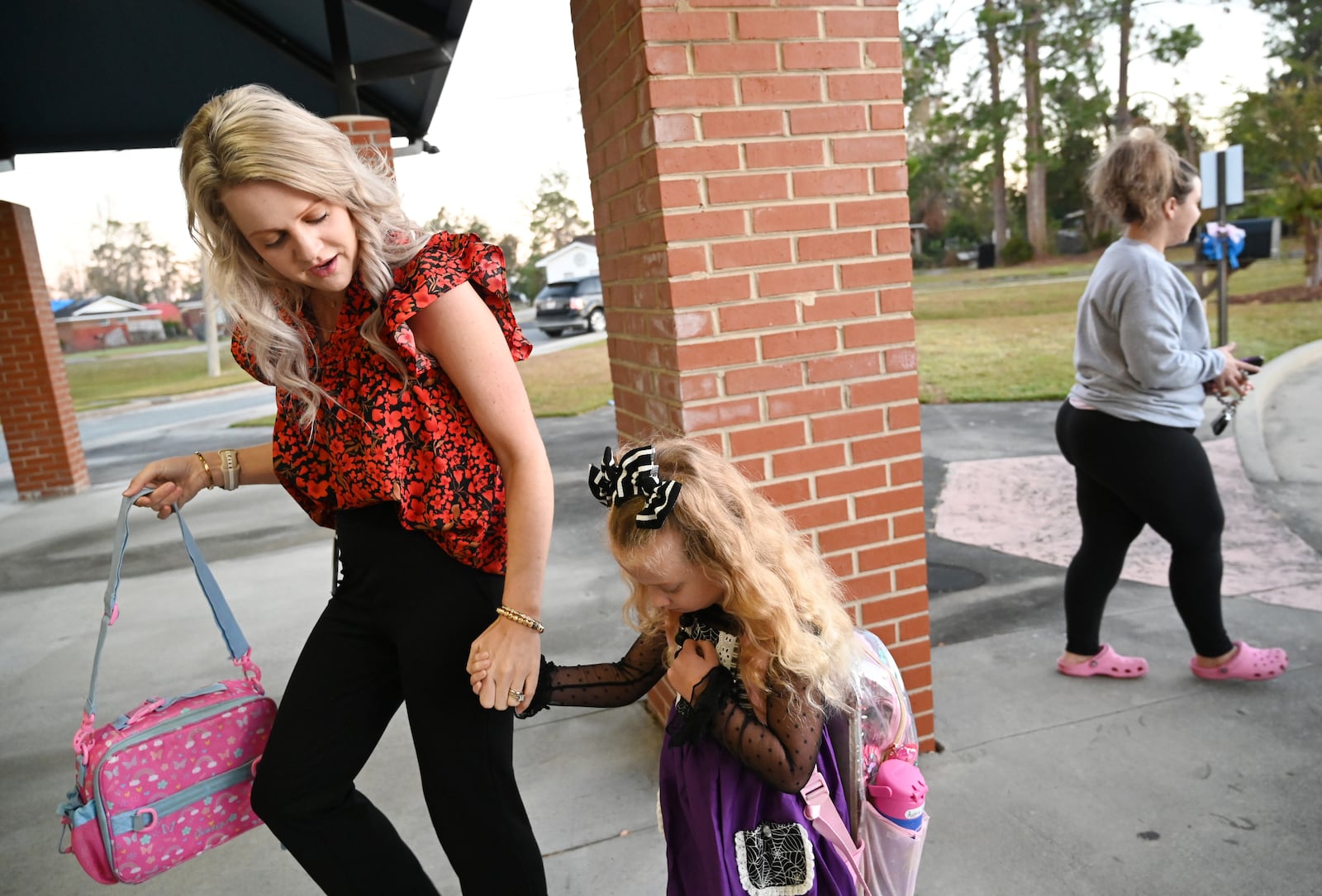 Principal Shelly McBride (left) welcomes Audrie Sharpe, 5, as her mother, Kenlie Sharpe (right), drops her off on Oct. 21 at Jeff Davis Primary School in Hazelhurst. Students returned for the first time since Hurricane Helene devastated much of South Georgia. (Hyosub Shin/AJC)