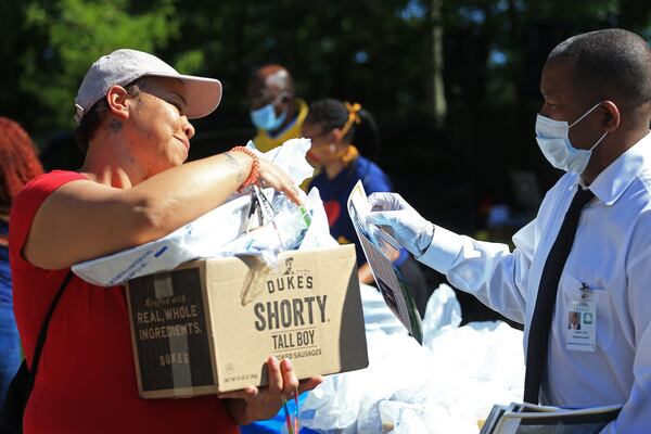 Joe Carn (right), Fulton County District 6 commissioner, hands a booklet to Danyell Vaughn during the Grab and Go free food and groceries event on Friday, April 17, 2020, at Allen Hills Apartments in Atlanta, which was organized to feed families during the coronavirus pandemic. (Christina Matacotta, for The Atlanta Journal-Constitution)