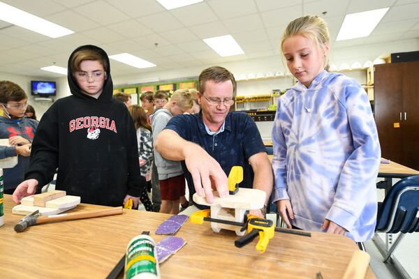 Fourth grade students Luke Wilson, 10 (left), and Madison Watford, 9, look on as instructor Scott Selvig (center) demonstrates how to clamp boards at Mountain Park Elementary School on Nov. 10, 2021. (Daniel Varnado/ For the Atlanta Journal-Constitution)