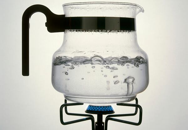 A photo of water boiling in a glass carafe on a gas ring. 