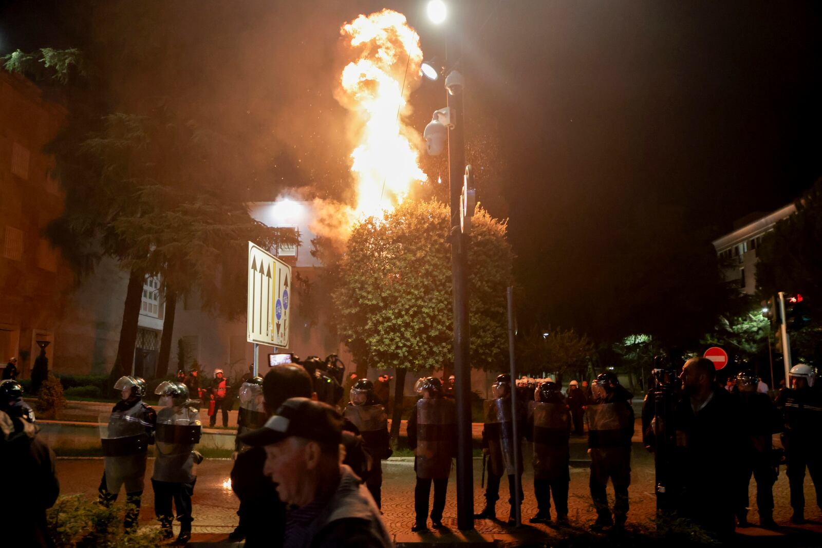 Fire burns behind a riot police cordon during an anti-government rally set up by the opposition, in Tirana, Albania, Monday, Oct. 7, 2024. (AP Photo/Hameraldi Agolli)