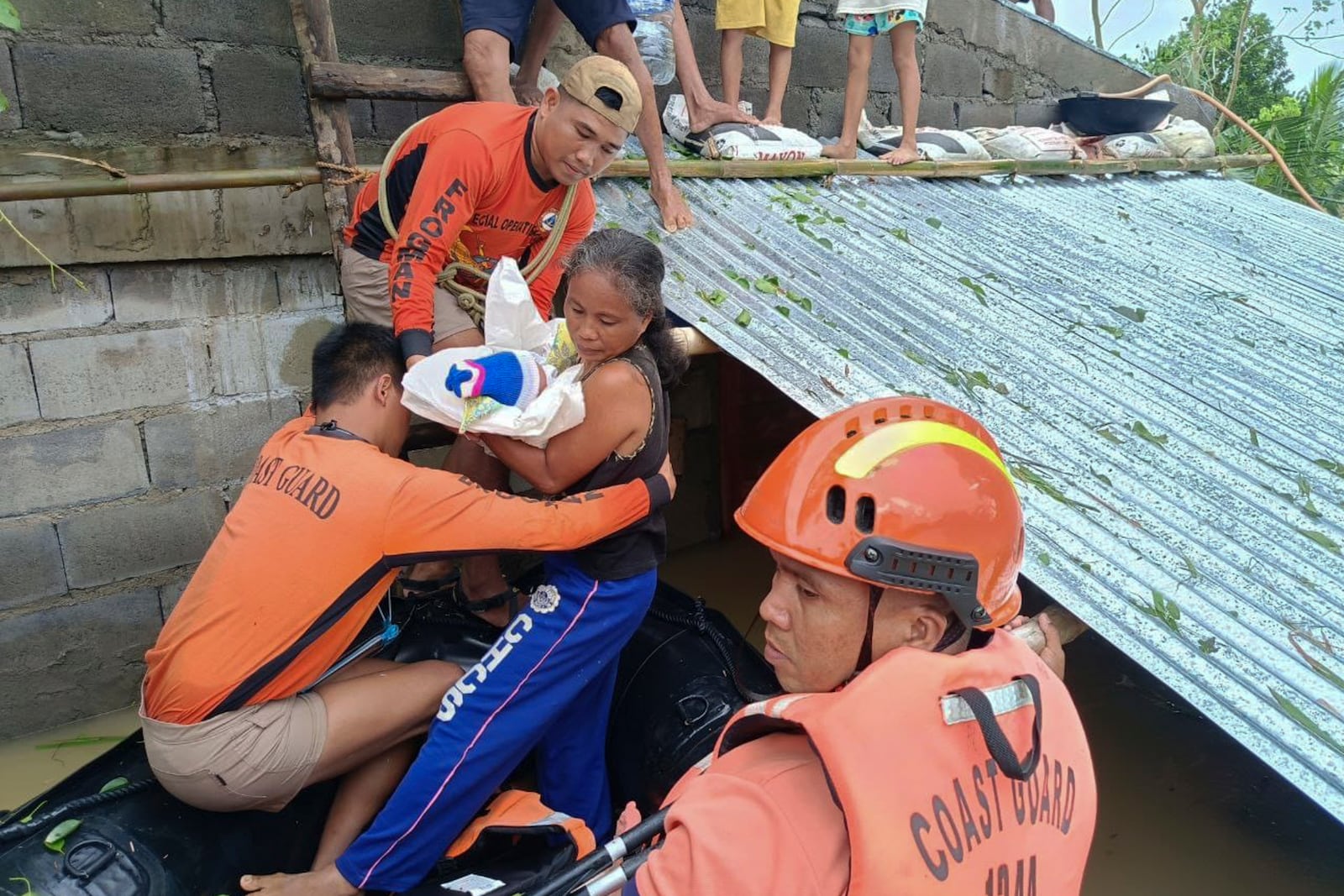 In this photo provided by the Philippine Coast Guard, a resident carries a baby as they are rescued from their roofs where they were staying to avoid floods caused by Tropical Storm Trami, locally named Kristine, at Libon, Albay province, Philippines on Wednesday Oct. 23, 2024. (Philippine Coast Guard via AP)