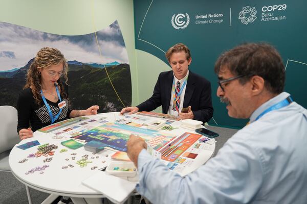 Courtney Howard, of Global Climate and Health Alliance and Nathan Cogswell, of World Resources Institute, center, play Daybreak, a game where players are supposed to work together to find a way to curb climate change, with Seth Borenstein, Associated Press science writer, at the COP29 U.N. Climate Summit, Tuesday, Nov. 19, 2024, in Baku, Azerbaijan. (AP Photo/Joshua A. Bickel)