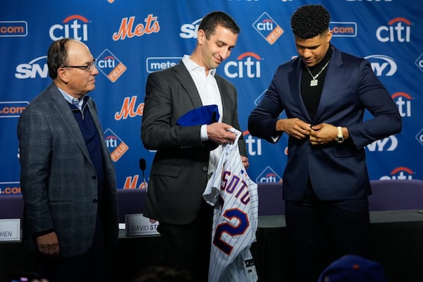 New York Mets owner Steven Cohen, left, looks on as new Mets plyaer Juan Soto, right, is presented with a jersey by the team's president of baseball operations David Stearns, center, during a news conference, Thursday, Dec. 12, 2024, in New York. (AP Photo/Frank Franklin II)