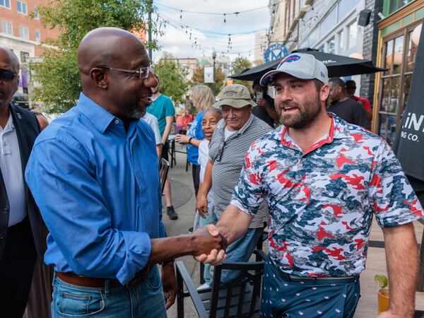 U.S. Sen. Raphael Warnock’s huge fundraising advantage has helped him dominate the airwaves in the closing stretch of the runoff election against Republican Herschel Walker. In the photo, Warnock (left) greets a supporter in Macon on Nov. 7, 2022. (Arvin Temkar /AJC)