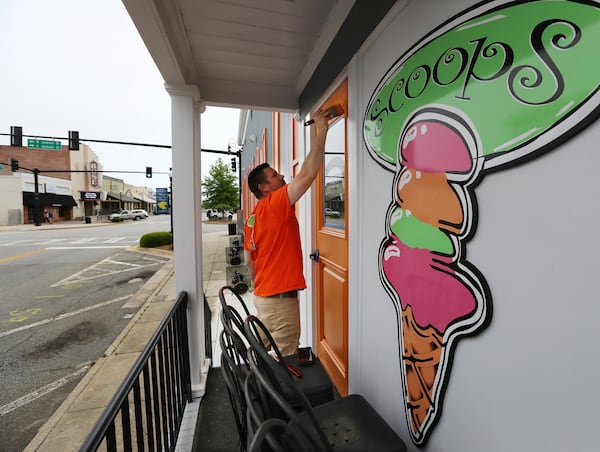 Brian Lambert paints a door as he gets ready to reopen Scoops, the ice cream shop he and his wife, Christie, own in Forsyth. They plan to take advantage of Gov. Brian Kemp’s order to allow some of the state’s businesses to reopen Friday after they have been shuttered in the midst of the coronavirus pandemic. “We have to open our doors, or our business will go under,” Christie Lambert said. Curtis Compton ccompton@ajc.com