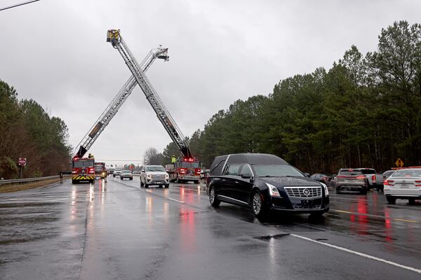 The hearse carrying the remains of Gwinnett County correctional officer Scott Riner goes underneath Gwinnett County fire trucks during the procession for Riner on Buford Drive, Tuesday, December 20, 2022, in Lawrenceville, Ga.. (Jason Getz / Jason.Getz@ajc.com)