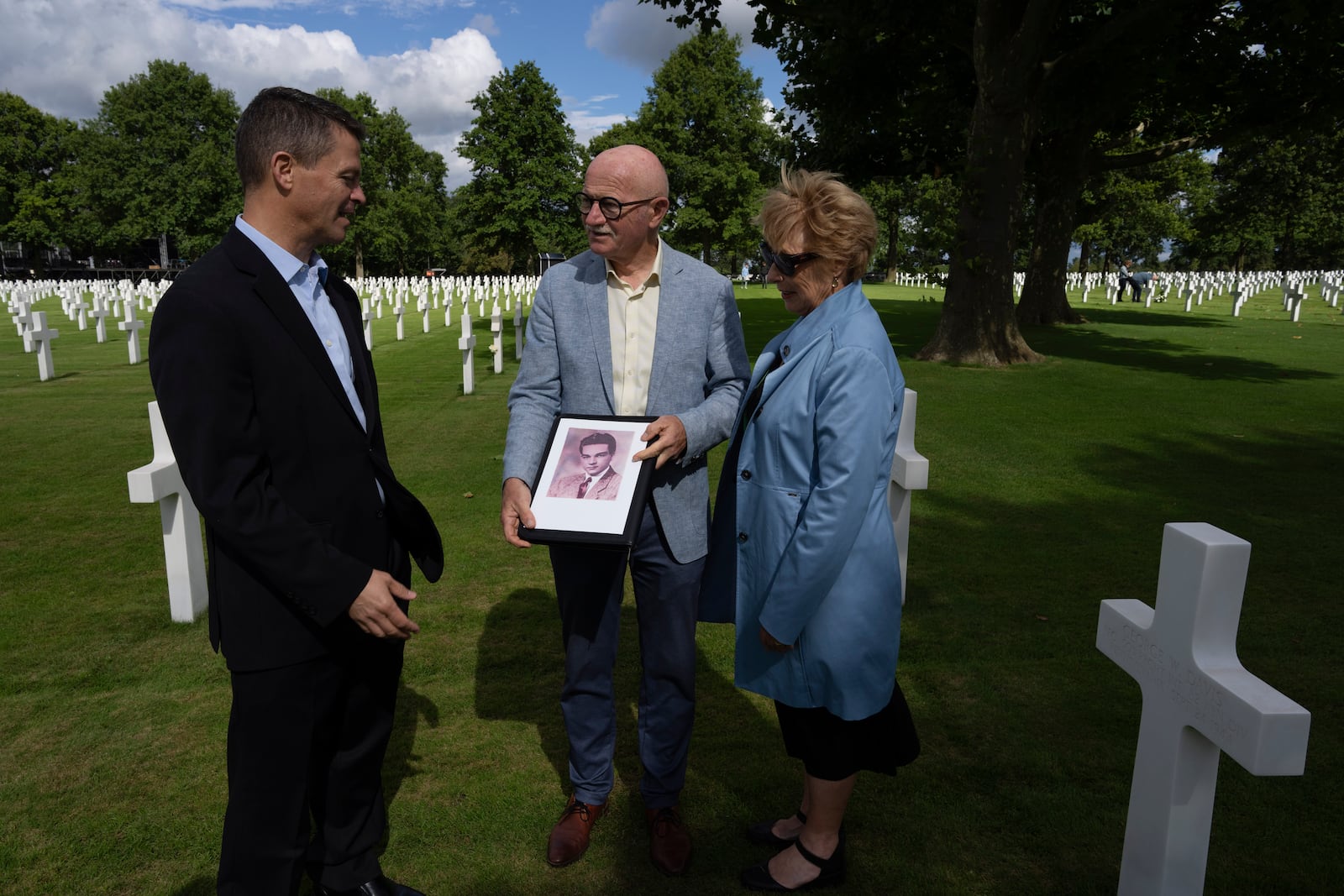 Eighty years after the liberation of the south of the Netherlands, Scott Taylor, left, Ton Hermes, center, and Maria Kleijnen, left, talk as they look at a picture of Scott's grandfather Second Lt. Royce Taylor, a bombardier with the 527 Bomb Squadron, at the Netherlands American Cemetery in Margraten, southern Netherlands, on Wednesday, Sept. 11, 2024. (AP Photo/Peter Dejong)