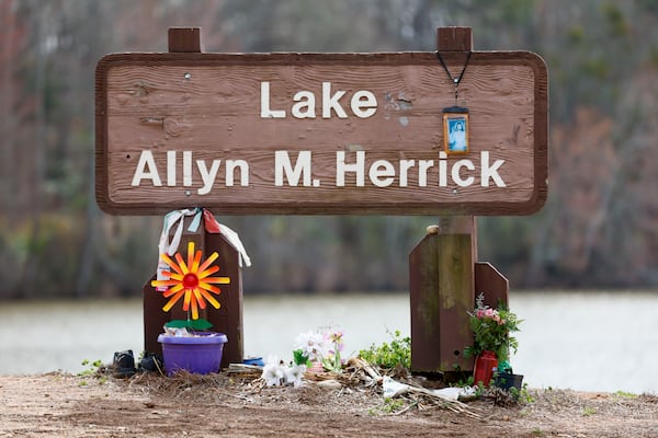 Flowers and multiple items are displayed around the sign at Lake Allyn M. Herrick Park in memory of Laken Riley, the nursing student who was murdered one year ago at the intramural trails. The University of Georgia has implemented increased security measures, including installing call boxes and video cameras. (Miguel Martinez/AJC)