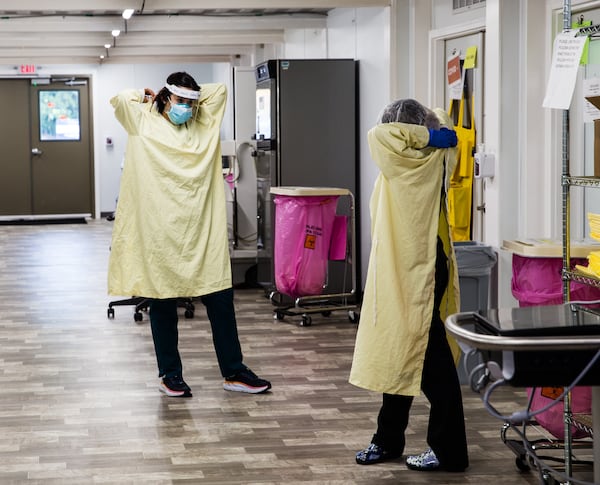 In a mobile medical unit provided by the state to Northeast Georgia Medical Center, patient care technicians Gabriela Estrada, left, and Soledad Santana, take off sterile gowns after checking on a patient. The mobile unit has helped with capacity problems, but hasn’t solved them, a hospital official told the AJC. (Jenni Girtman for The Atlanta Journal Constitution)