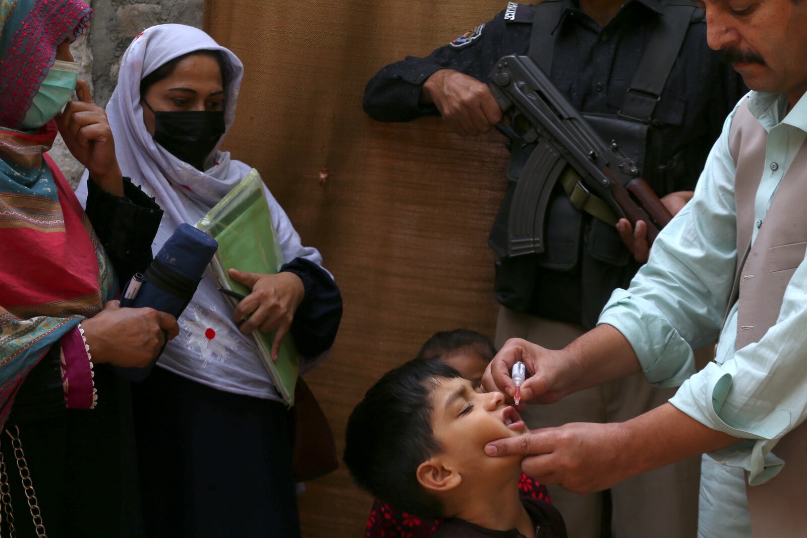 A police officer stands guard as a health worker, right, administers a polio vaccine to a child in a neighbourhood of Peshawar, Pakistan, Monday, Oct. 28, 2024. (AP Photo/Mohammad Sajjad)