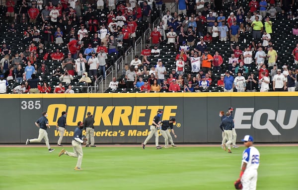 Braves grounds crew members clear up debris on the field thrown by disgruntled Braves fans after Philadelphia Phillies third baseman Alec Bohm (28) scored on a disputed call in the ninth inning Sunday, April 11, 2021, at Truist Park in Atlanta. (Hyosub Shin / Hyosub.Shin@ajc.com)