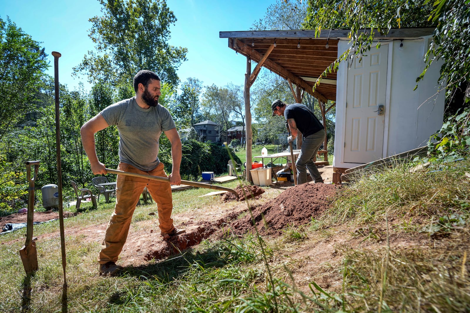 Volunteers, Ben Gordon, left, and Anthony Rubino work on digging a ditch for pipes to offer both nonpotable and potable water for the community, Monday, Oct. 14, 2024, in Asheville, N.C. (AP Photo/Kathy Kmonicek)