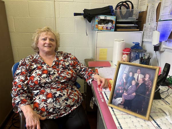 Carolyn Johnson poses for a photo in the Hunter's Livermush office with a portrait of her family. (Olivia Wakim for The Atlanta Journal-Constitution)